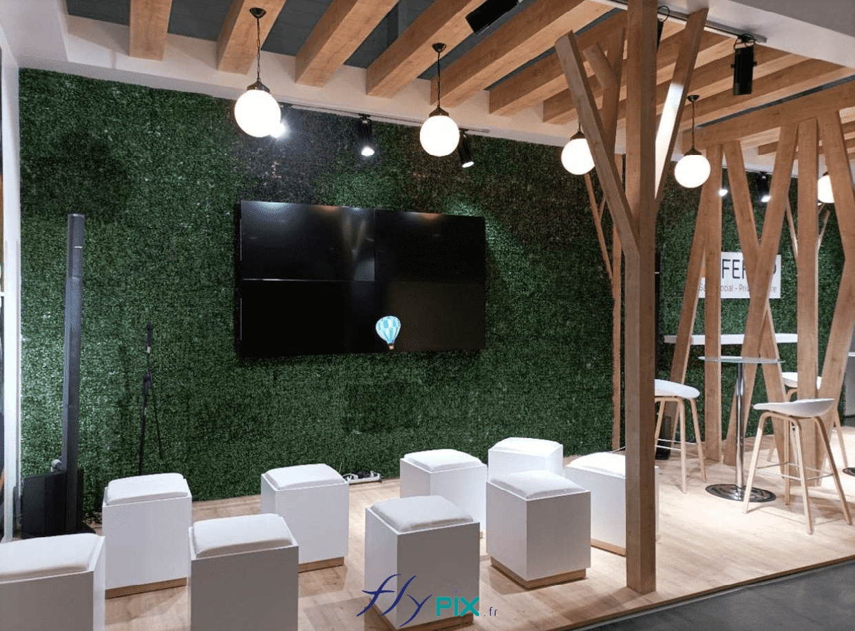 FEHAP : vue en modélisation en 3D, prévisualisation du concept de l'intérieur du stand menuiserie : écran TV, sièges, bois, sol en lino, lampadaires et lumières.