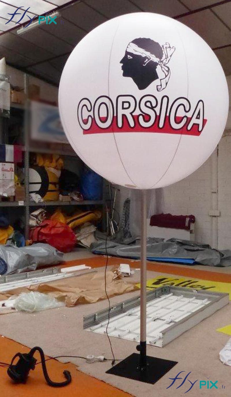 Vue générale du ballon sur mat imprimé CORSICA, gonflé à l'air avec une pompe électrique, et avec son pied stabilisateur en métal au sol.